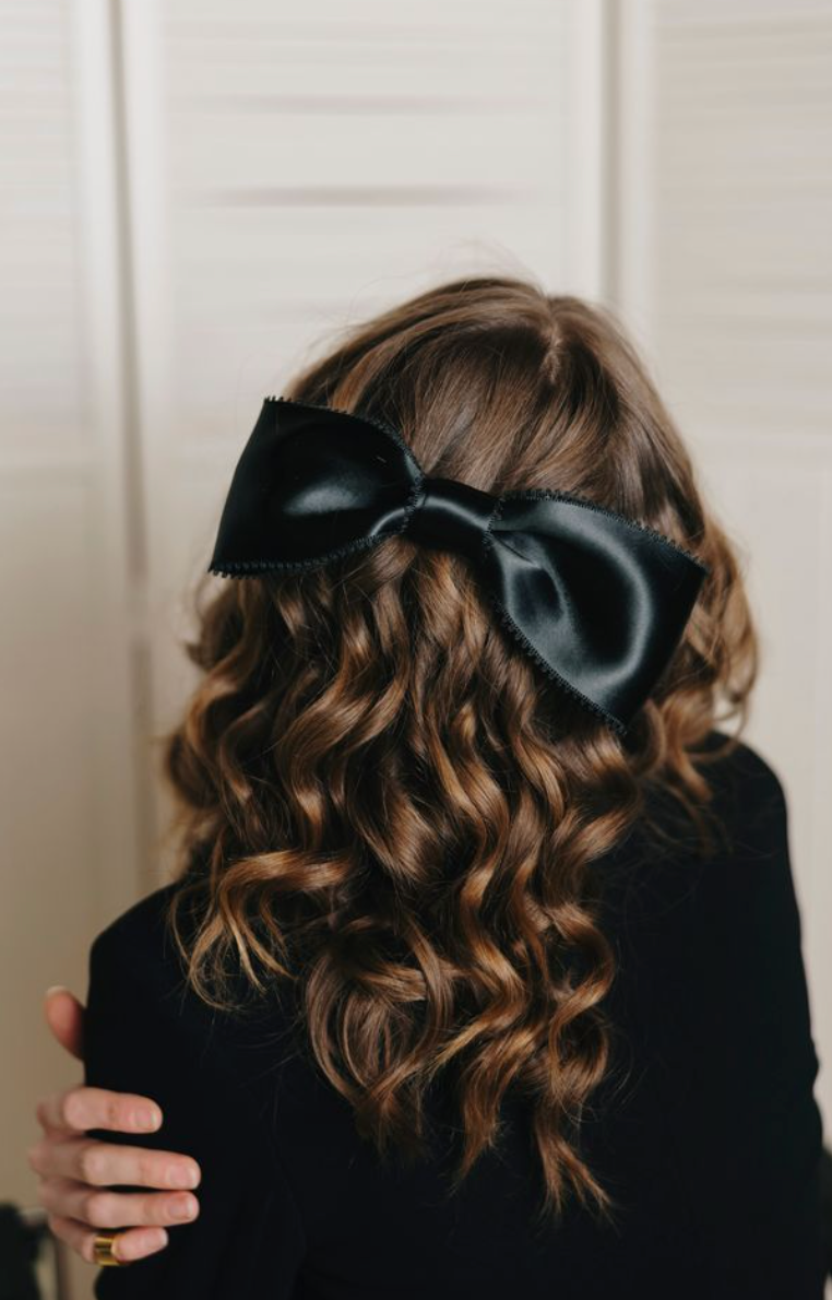 Person with wavy hair wearing a large black bow, against a neutral background