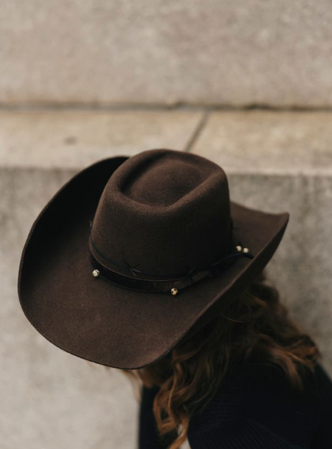 Brown cowboy hat with decorative band on a textured surface
