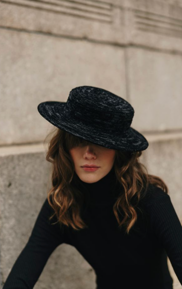 Person wearing a black hat and black turtleneck against a neutral wall