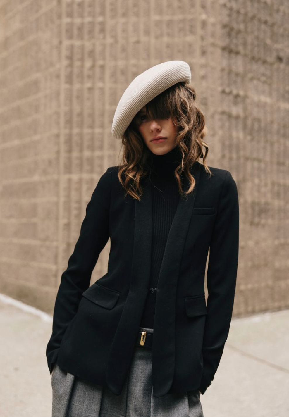 Person wearing a black coat and white beret against a brick wall.