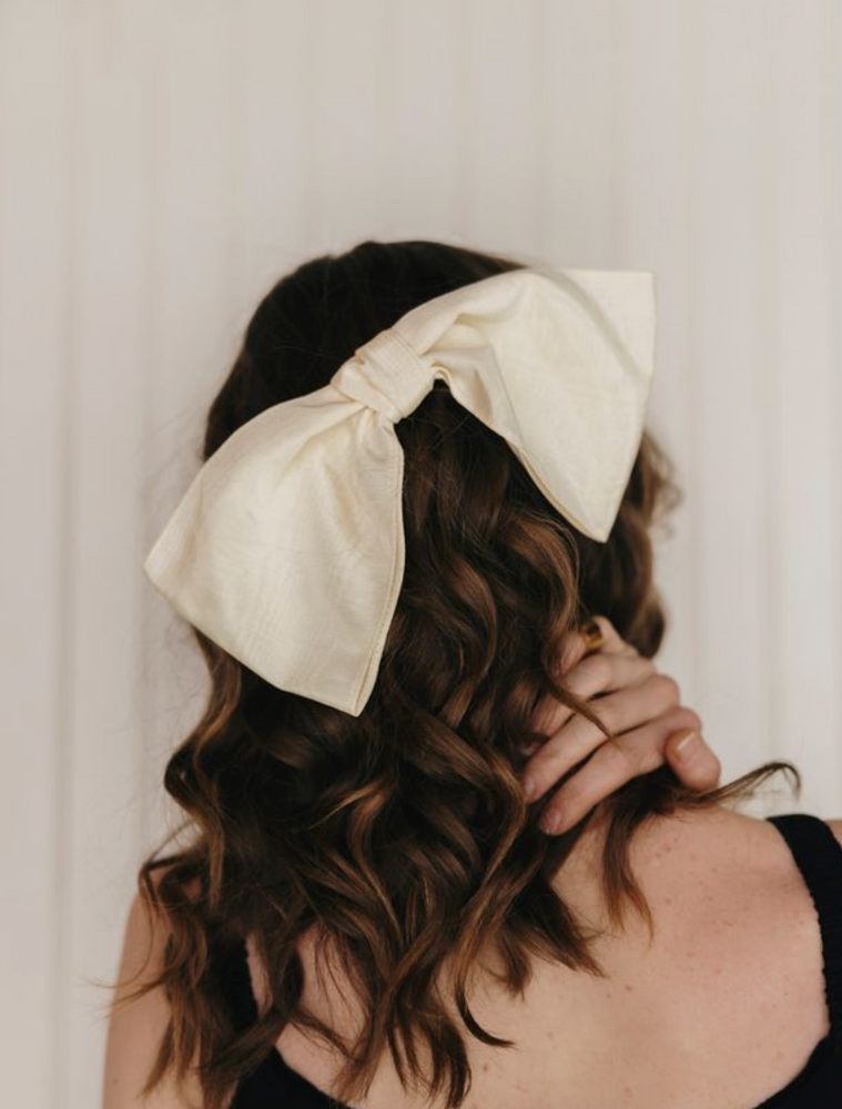 Woman wearing a large cream-colored bow headband against a neutral background